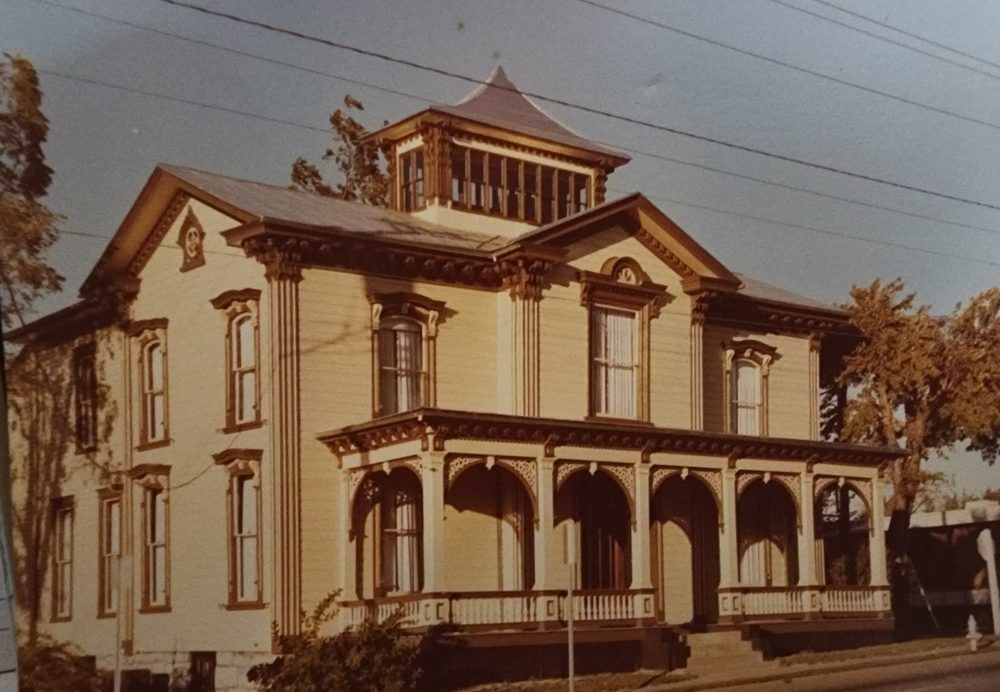 Historic Victorian-style house with ornate detailing and wraparound porch, surrounded by trees.