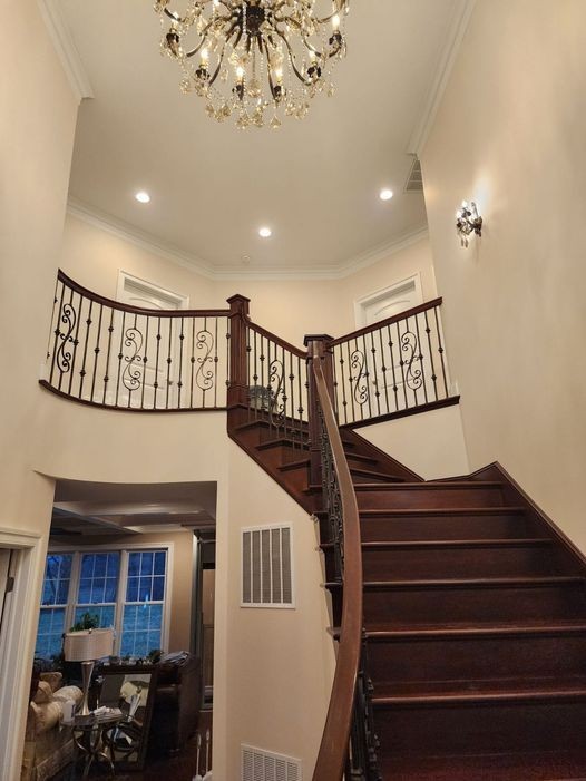 Elegant spiral staircase in a home with wooden steps and decorative railing, beneath a chandelier.